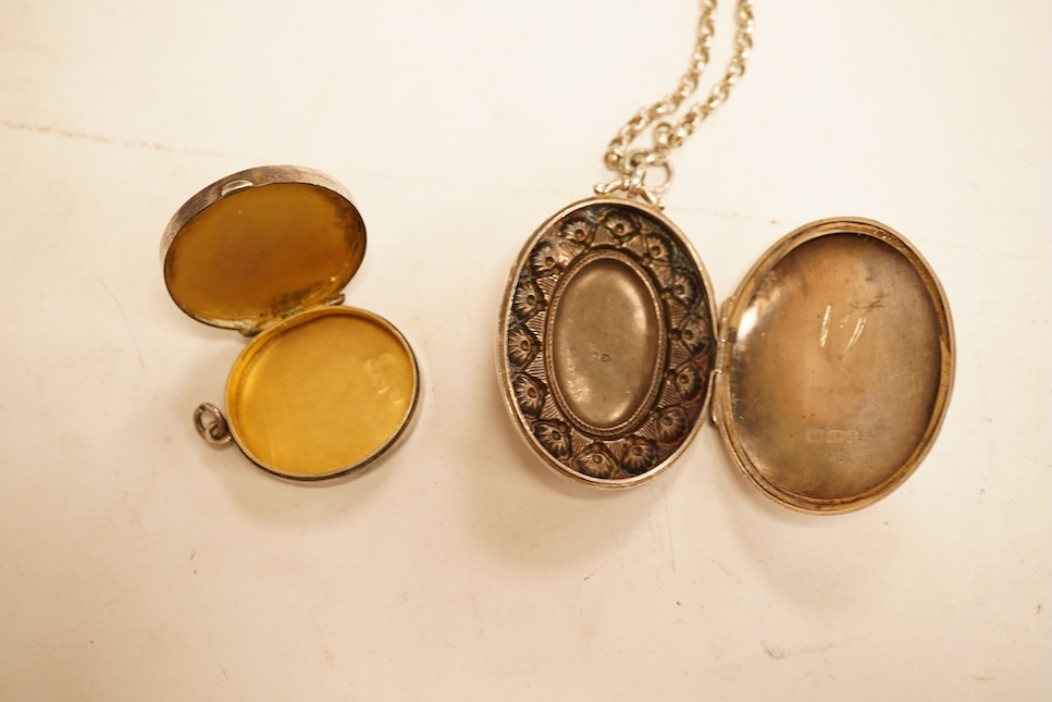 A late Victorian embossed and engraved oval silver locket, 42mm, on a later white meta belcher link chain, together with an Edwardian silver and hardstone inlaid pill box, now with pendant mount.